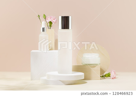Cosmetic glass jars with natural cream, face serum and organic tonic on podiums on pink background with pink flowers. Organic beauty product and skin friendly cosmetics concept. Mockup, front view 128466923