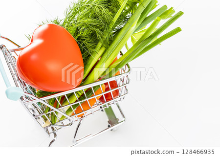 Healthy food concept. Natural vegetables with red heart in shopping trolley on white table. Vegetarian and vegan diet Healthy food concept. Natural vegetables with red heart in shopping trolley on white table. Vegetarian and vegan diet 128466935