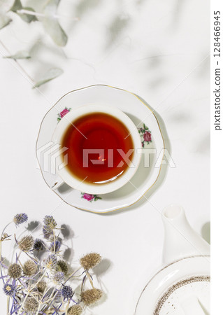 Tea time. Healing natural herbal tea with wild plants and flowers. Sustainable morning composition with cup of tea, teapot and dry flowers on white background. Flat lay, vertical format 128466945