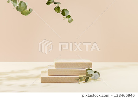 Wooden empty square podium for presentation or advertising. Product display on pink background with green eucalyptus leaves and shadows. Concept of scene stage for beauty products or promotion sale 128466946