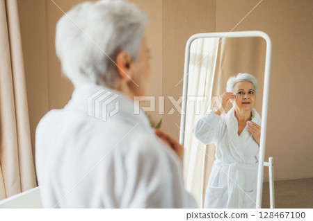 Love yourself. Beautiful old woman enjoying mirror reflection. Senior older lady spending morning in bathroom looking at mirror confident happy. Woman doing daily morning beauty routine. Self love 128467100