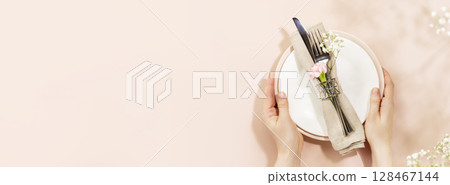 Female hands hold holiday dishes on light pink background with spring white flowers and shadows. Romantic holiday table settings. Flat lay, banner size, copy space 128467144