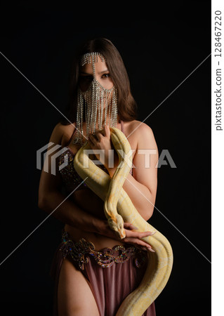 Woman poses elegantly in studio while playfully interacting with a snake Woman poses elegantly in studio while playfully interacting with a snake 128467220