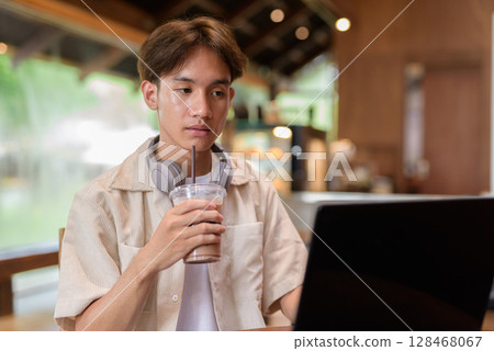 Handsome young non binary man sitting in cafe restaurant using laptop computer Handsome young non binary man sitting in cafe restaurant using laptop computer 128468067