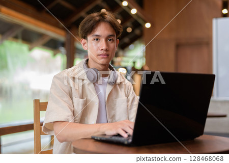 Handsome young non binary man sitting in cafe restaurant using laptop computer Handsome young non binary man sitting in cafe restaurant using laptop computer 128468068