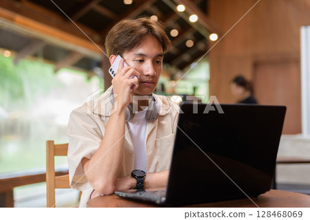 Handsome young non binary man sitting in cafe restaurant using laptop computer 128468069