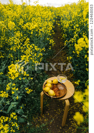 Relaxing by a vibrant yellow flower field with pastries and lemons on a wooden table 128468083