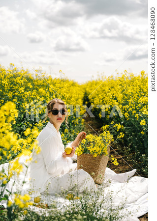 Woman in white attire gathers yellow flowers in a blooming field under a cloudy sky Woman in white attire gathers yellow flowers in a blooming field under a cloudy sky 128468090