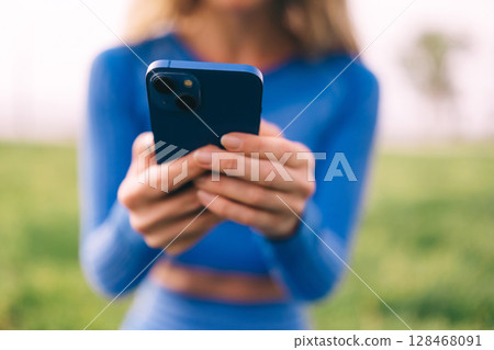 Fitness woman using mobilephone while exercising. Smiling woman doing stretching workout  128468091