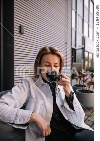 Woman enjoying coffee outdoors at a modern cafe in the afternoon 128468099