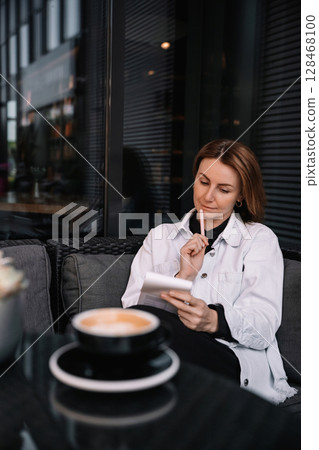 Woman enjoying coffee while reading notes in a cozy cafe setting during the afternoon Woman enjoying coffee while reading notes in a cozy cafe setting during the afternoon 128468100