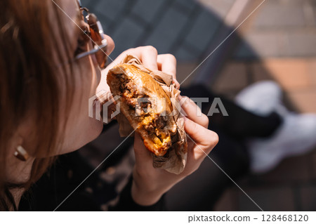 Enjoying a delicious burger outdoors at a sunny park during lunchtime with friends 128468120