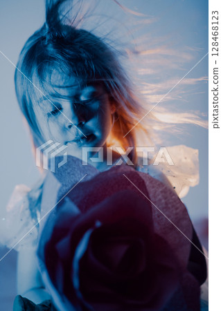 Young girl holds a rose in artistic lighting with flowing hair and a thoughtful expression 128468123