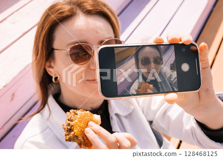 Woman enjoys gourmet food while taking a selfie in a colorful outdoor setting 128468125