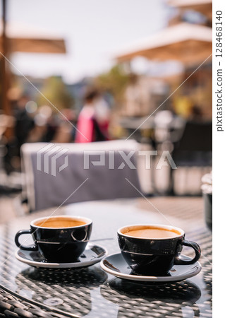 Two cups of coffee on a table in an outdoor cafe under bright sunlight 128468140