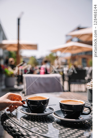 Enjoying coffee in a bustling outdoor cafe on a sunny afternoon Enjoying coffee in a bustling outdoor cafe on a sunny afternoon 128468144