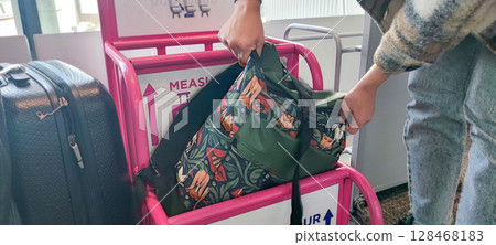 Person fitting bag into airport baggage sizer (pink frame). Carry-On Bag Airport Sizer Check - Travel Essentials, Hand Luggage, Budget Airline Rules 128468183