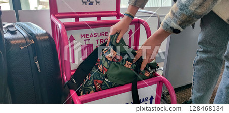 Person fitting bag into airport baggage sizer (pink frame). Carry-On Bag Airport Sizer Check - Travel Essentials, Hand Luggage, Budget Airline Rules 128468184