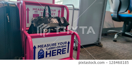 Person fitting bag into airport baggage sizer (pink frame). Carry-On Bag Airport Sizer Check - Travel Essentials, Hand Luggage, Budget Airline Rules 128468185