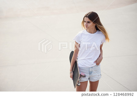 Young pretty girl in a white t-shirt and denim shorts holding skateboard. Young pretty girl in a white t-shirt and denim shorts holding skateboard. 128468992