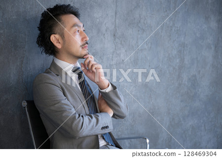 A businessman in a suit sitting in a chair thinking. A profile of an image of success, goals, tactics and strategy planning 128469304