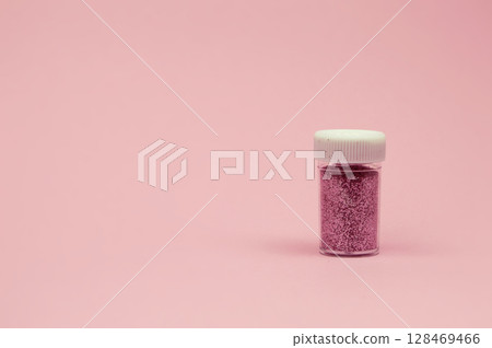 A glass jar brimming with fine pink shimmer is placed on a soft pink surface, glowing with light in a detailed close-up. A glass jar brimming with fine pink shimmer is placed on a soft pink surface, glowing with light in a detailed close-up. 128469466