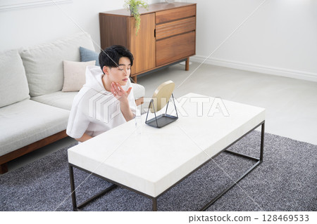 A man checking his skin care in the mirror. The reflection of his face in the mirror creates a bright, clean, and lively image. A man checking his skin care in the mirror. The reflection of his face in the mirror creates a bright, clean, and lively image. 128469533