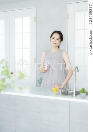 Middle-aged woman drinking water in the kitchen Middle-aged woman drinking water in the kitchen 128469857