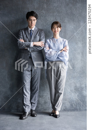 Full body of business men and women in suits on a gray background, arms crossed, serious expressions looking at the camera 128470294