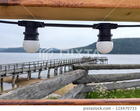 lamps illuminate tranquil lakeside pier at dusk, surrounded by gentle mountains. closeup. 128470733