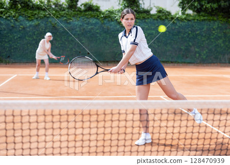 Middle aged and senior women plays tennis on open court with opponent. Middle aged and senior women plays tennis on open court with opponent. 128470939