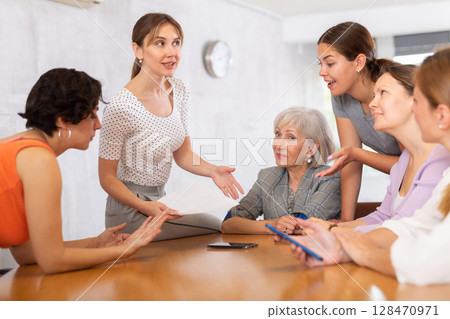 young girl student sits on table near friends and promotes version of solution of educational task 128470971