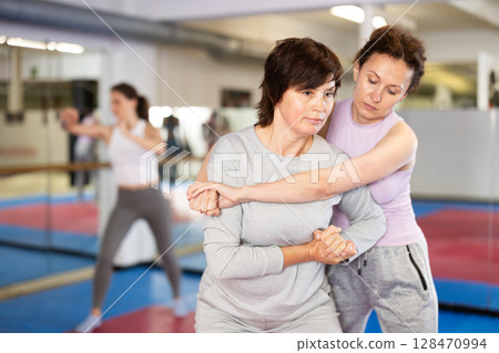 Emotional woman trying to escape from back grip and delivering elbow strike to midsection to female opponent during mock bout in self defense training Emotional woman trying to escape from back grip and delivering elbow strike to midsection to female opponent during mock bout in self defense training 128470994