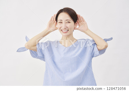 Woman, middle-aged, gesture of listening with hand on ear, white background, looking at camera 128471056
