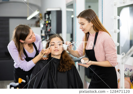 Professional women makeup artists applying shadows and blush to young client 128471120