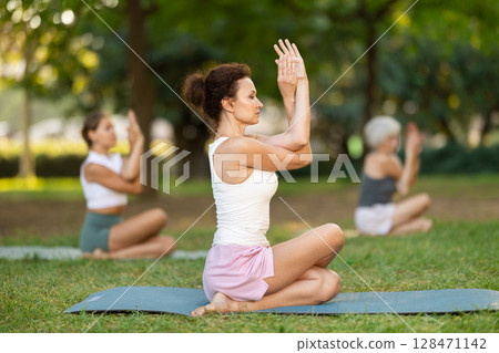 Woman performing Gomukhasana Garudasana outdoors with group 128471142