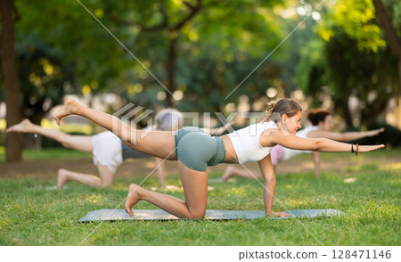 Girl performing balancing table asana during group yoga in park 128471146