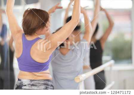 Rear view of woman practicing ballet postures at amateur group rehearsal 128471172