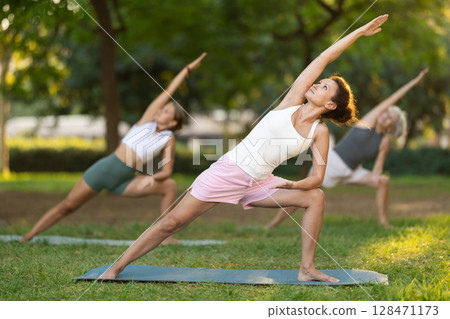 Woman performing Utthita Parsvakonasana at group yoga session in park 128471173