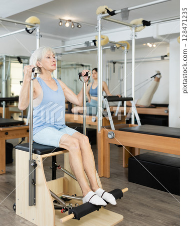 Aged woman exercising on wunda chair in pilates studio 128471235