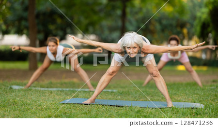 Young and mature women practicing different poses during group yoga training at park together 128471236