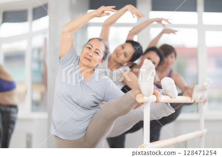 Aged woman stretching at barre in group ballet class Aged woman stretching at barre in group ballet class 128471254