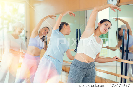 Slim women practicing ballet at ballet barre with choreographer 128471257