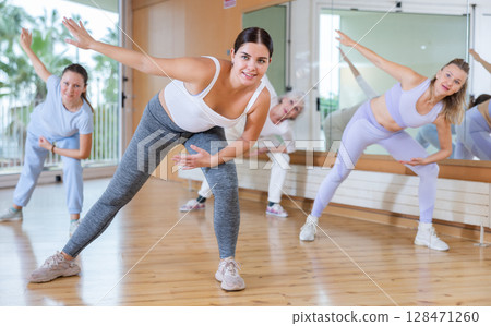 Happy flexible women of different ages exercising active dance with sliding leg to side in fitness center Happy flexible women of different ages exercising active dance with sliding leg to side in fitness center 128471260