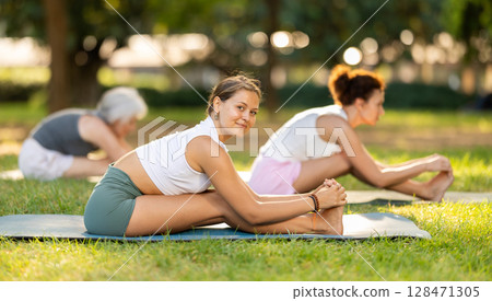 Girl enjoying yoga session on green glade with friends Girl enjoying yoga session on green glade with friends 128471305