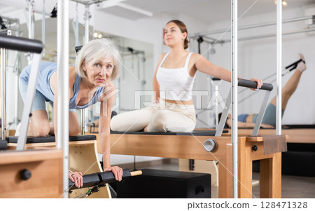 Elderly woman in sportswear training pilates performer bed in gym 128471328