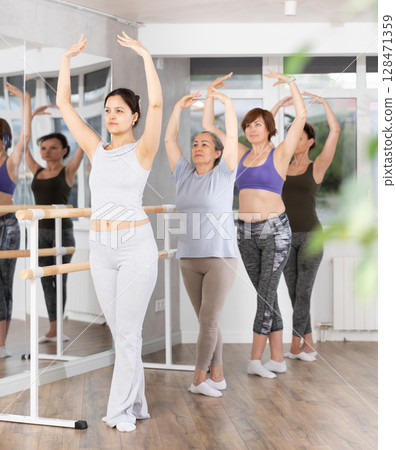 Woman practicing fifth ballet position with group of female amateurs 128471359