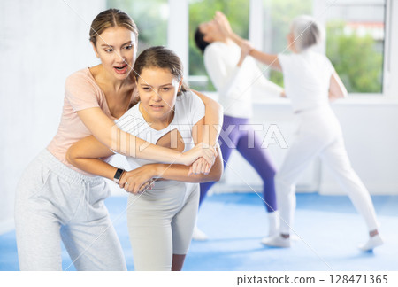 Woman escaping from back grip and delivering elbow strike to midsection in self-defense training Woman escaping from back grip and delivering elbow strike to midsection in self-defense training 128471365