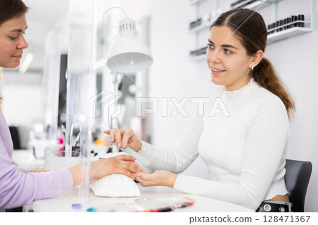 Friendly manicurist files the nails of a young female client Friendly manicurist files the nails of a young female client 128471367