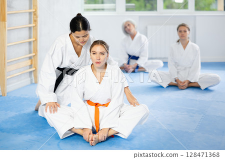 Young woman in kimono performing butterfly stretch with female coach Young woman in kimono performing butterfly stretch with female coach 128471368